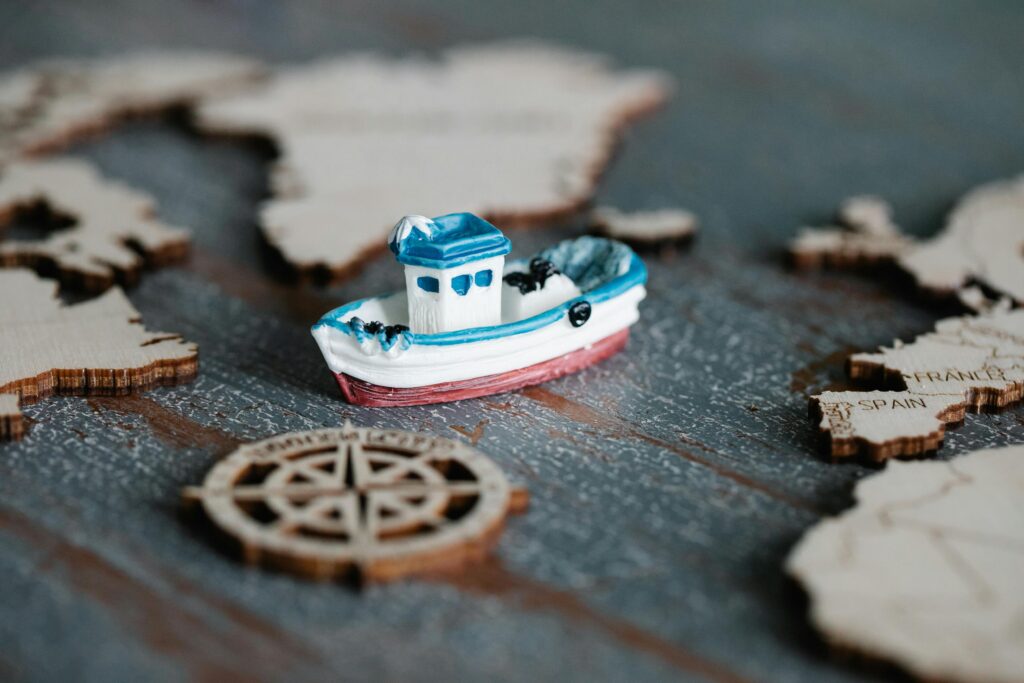 A close-up of a toy boat on a wooden map with a compass, representing travel and navigation.