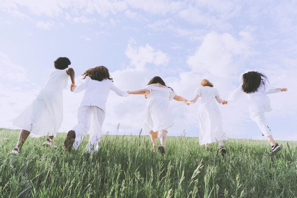 Five women joyfully running in a field under a clear sky, symbolizing freedom and happiness.